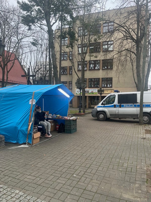 Zdjęcie przedstawiające punkt sprzedaży fajerwerków oraz sprzedawcę. W tle widać radiowóz policyjny.