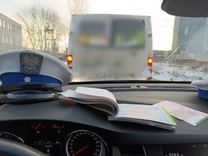Zdjęcie poglądowe wykonane wewnątrz radiowozu. Na zdjęciu widać czapkę policyjną, bloczek mandatowy, a przed radiowozem pojazd dostawczy.