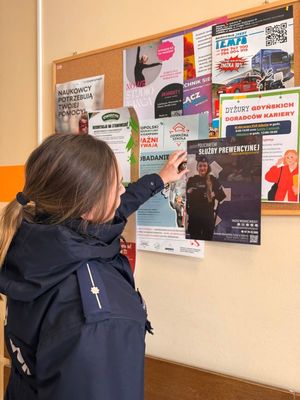 Zdjęcie przedstawiające dzielnicową, przywieszającą plakat, dotyczący naboru do Policji.