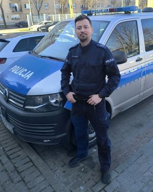 Zdjęcie przedstawiające policjanta stojącego przy radiowozie.