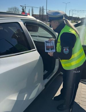 Zdjęcie przedstawiające policjantkę podczas kontroli pojazdu. Na zdjęciu widać, jak policjantkę przy pojeździe z broszurami reklamującymi kampanię.
