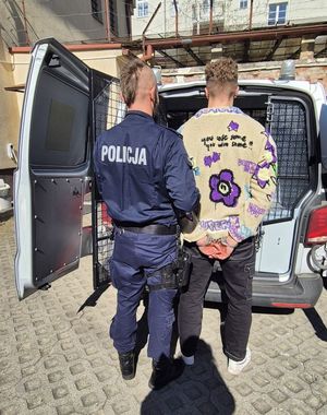 Zdjęcie przedstawiające policjanta z zatrzymanym mężczyzną przy radiowozie.