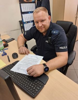 Zdjęcie przedstawiające policjanta siedzącego przy biurku.