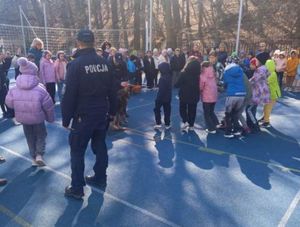 Zdjęcie przedstawiające policjanta oraz dzieci na boisku szkolnym.