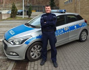 Zdjęcie przedstawiające policjanta stojącego na tle radiowozu.