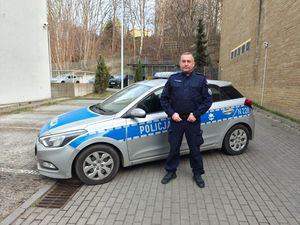 Zdjęcie przedstawiające policjanta stojącego na tle radiowozu.