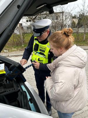 Zdjęcie przedstawiające kobietę, która w licytacji wygrała dzień w Komendzie Miejskiej Policji w Gdyni wraz z policjantem ruchu drogowego, który pokazuje, jak zrobić pomiar prędkości.