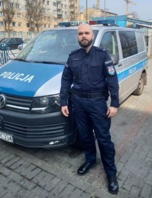 Zdjęcie przedstawiające policjanta na tle radiowozu.