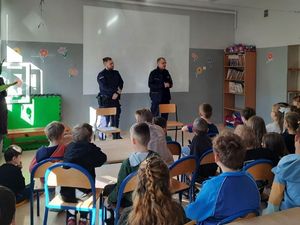 Zdjęcie przedstawiające dwóch policjantów, prowadzących zajęcia profilaktyczne z uczniami.
