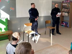 Zdjęcie przedstawiające dwóch policjantów, prowadzących zajęcia profilaktyczne z uczniami.