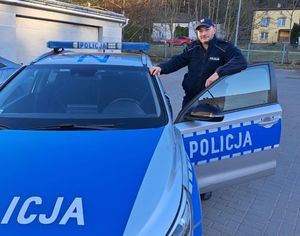 Zdjęcie przedstawiające policjanta, stojącego przy radiowozie.