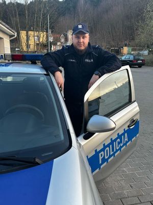 Zdjęcie przedstawiające policjanta stojącego przy radiowozie.