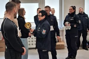 Zdjęcie przedstawiające p.o. Komendanta Miejskiego Policji w Gdyni mł. insp. Beatę Nienadowską podczas wręczania pucharu zwycięzcy konkurencji. Na zdjęciu widać również innych policjantów oraz uczestników zawodów.
