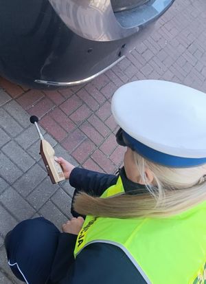 Zdjęcie poglądowe, przedstawiające policjantkę, która przy pojeździe trzyma w ręku sonometr.