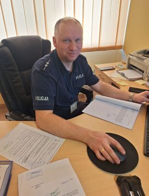 Zdjęcie przedstawiające policjanta siedzącego przy biurku.
