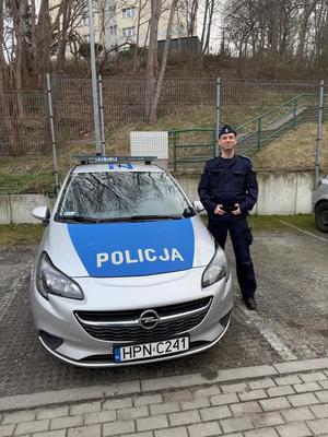 Zdjęcie przedstawiające policjanta, stojącego przy radiowozie.