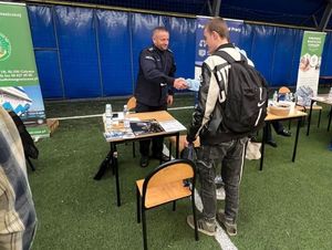 Zdjęcie przedstawiające policjanta podczas Targów Pracy. Policjant wita się z uczestnikiem targów.