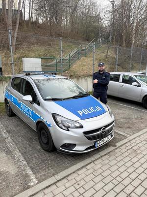 Zdjęcie przedstawiające policjanta, stojącego przy radiowozie.