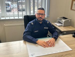 Zdjęcie przedstawiające policjanta, siedzącego przy biurku.