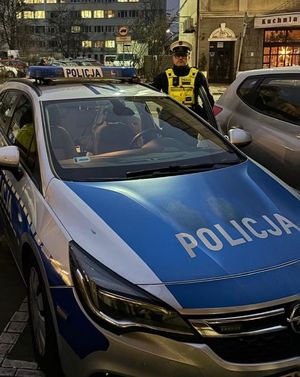 Zdjęcie przedstawiające umundurowanego policjanta, stojącego przy radiowozie.