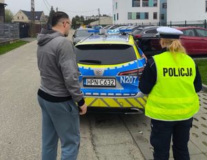 Zdjęcie przedstawiające policjanta poza służbą oraz umundurowaną policjantkę, stojących przy radiowozie.