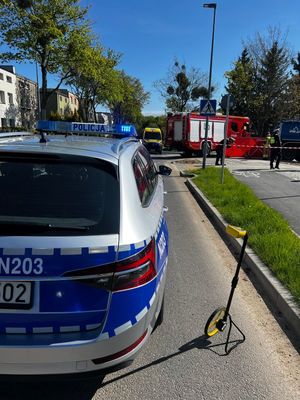 Zdjęcie przedstawiające policjantów ruchu drogowego podczas wykonywania czynności na miejscu wypadku. Na zdjęciu widać również radiowóz policyjny, wóz strażacki oraz karetkę pogotowia ratunkowego.