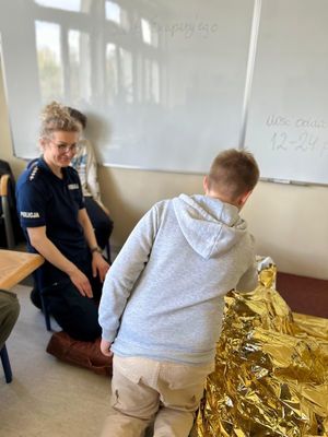 Zdjęcie przedstawiające policjantkę podczas prowadzenia zajęć praktycznych z czwartoklasistami z udzielania pierwszej pomocy medycznej.