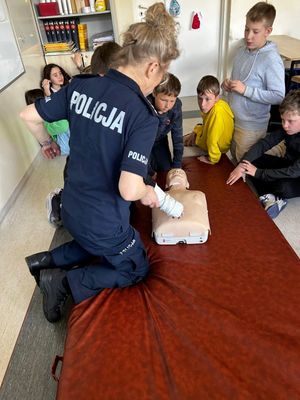 Zdjęcie przedstawiające policjantkę podczas prowadzenia zajęć praktycznych z czwartoklasistami z udzielania pierwszej pomocy medycznej.