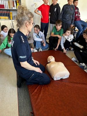 Zdjęcie przedstawiające policjantkę podczas prowadzenia zajęć praktycznych z czwartoklasistami z udzielania pierwszej pomocy medycznej.
