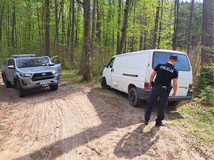Zdjęcie przedstawiające dzielnicowego na tle radiowozu Straży Leśnej oraz busa.