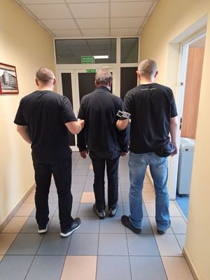 Zdjęcie przedstawiające policjantów prowadzących zatrzymanego mężczyznę.