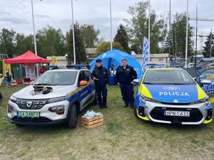 Zdjęcie przedstawiające policjantkę i strażnika miejskiego na tle radiowozów słuzbowych.