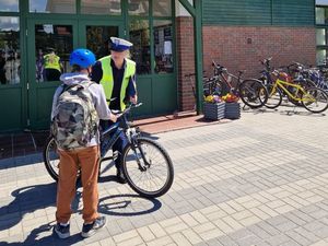 Zdjęcie przedstawiające policjantkę, która rozmawia z uczniem przed szkołą. Uczeń stoi przy rowerze.