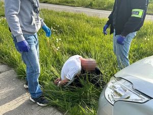 Zdjęcie przedstawiające siedzącego przed pojazdem zatrzymanego mężczyznę. Na zdjęciu widać dwóch kryminalnych, stojących przy mężczyźnie.