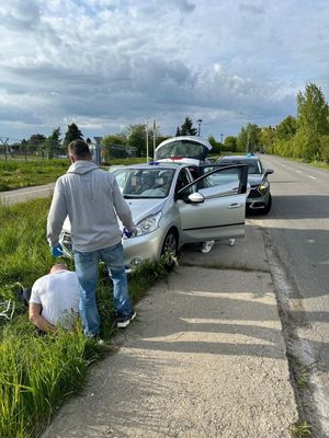 Zdjęcie przedstawiające siedzącego przed pojazdem zatrzymanego mężczyznę. Na zdjęciu widać policjanta, stojącego przy mężczyźnie oraz dwa pojazdy.