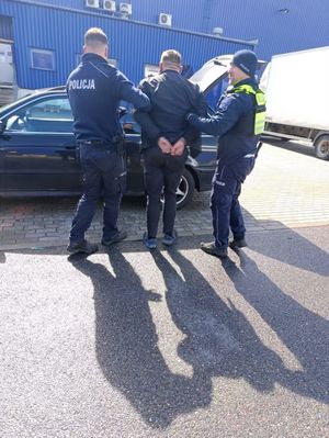 Zdjęcie przedstawiające dwóch policjantów prowadzących zatrzymanego mężczyznę.