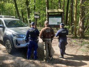Zdjęcie poglądowe, przedstawiające dwóch policjantów i strażnika leśnego na tle pojazdu Straży Leśnej.