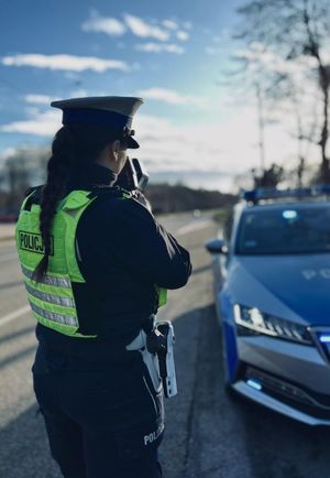 Zdjęcie przedstawiające policjantkę ruchu drogowego podczas wykonywania pomiaru prędkości.