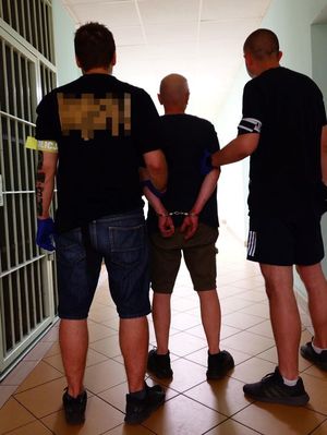 Zdjęcie przedstawiające policjantów, prowadzących zatrzymanego mężczyznę.