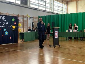 Zdjęcie przedstawiające pełniącego obowiązki Naczelnika Wydziału Prewencji Komendy Miejskiej Policji w Gdyni podczas przemówienia w V LO. W tle widać uczniów szkoły.
