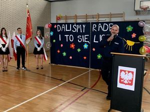 Zdjęcie przedstawiające pełniącego obowiązki Naczelnika Wydziału Prewencji Komendy Miejskiej Policji w Gdyni podczas przemówienia w V LO. W tle widać uczniów szkoły.
