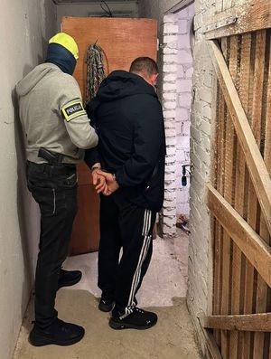 Zdjęcie przedstawiające policjanta z zatrzymanym mężczyzną w pomieszczeniu piwnicznym.