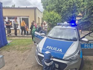 Zdjęcie przedstawiające dzieci przy radiowozie oraz w tle innych uczestników festynu.