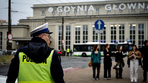 Zdjęcie przedstawiające policjanta na tle budynku dworca głównego w Gdyni.