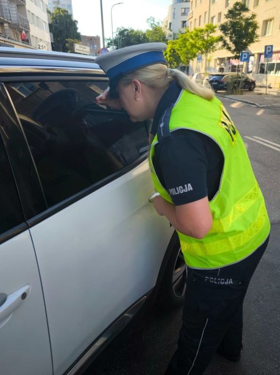 Zdjęcie przedstawiające policjantkę zaglądającą przez szybę do wnętrza samochodu.