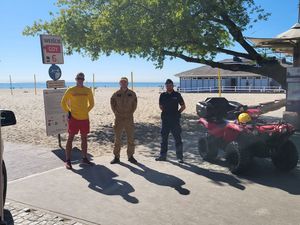 Zdjęcie przedstawiające policjanta, funkcjonariusza Państwowej Straży Pożarnej oraz ratownika WOPR przy wejściu na plaże miejską nr 6.
