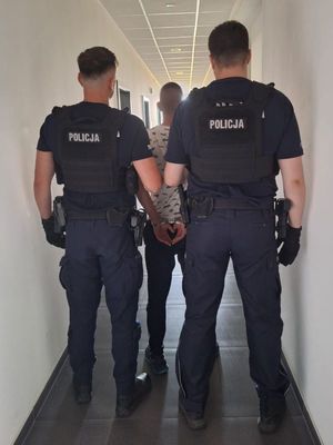 Zdjęcie przedstawiające policjantów prowadzących zatrzymanego mężczyznę.