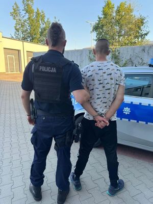 Zdjęcie przedstawiające policjanta prowadzącego zatrzymanego mężczyznę.