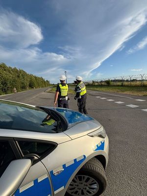 Zdjęcie przedstawiające policjantów ruchu drogowego na tle radiowozu.