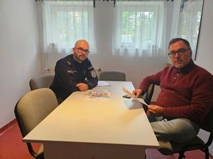 Zdjęcie przedstawiającego dzielnicowego i przewodniczącego rady dzielnicy, siedzących przy stole w placówce Rady Dzielnicy Wzgórze Świętego Maksymiliana.